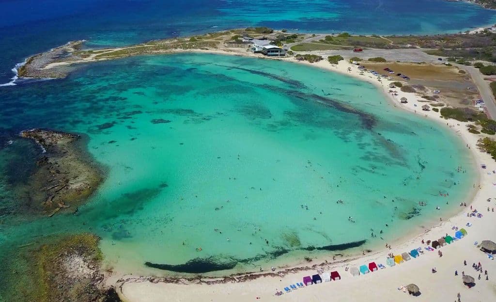 Aerial view of a beach featuring clear blue water and sandy shores under a bright sky