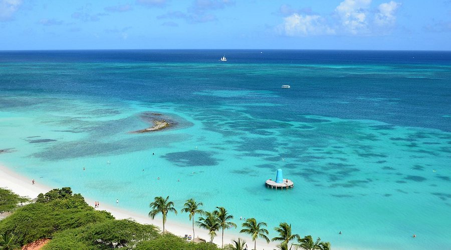 sunny beach scene featuring a boat and people swimming in the clear water.