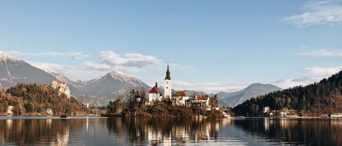 Aerial view of Bled Island, surrounded by the serene waters of Lake Bled, with lush greenery and a church steeple visible