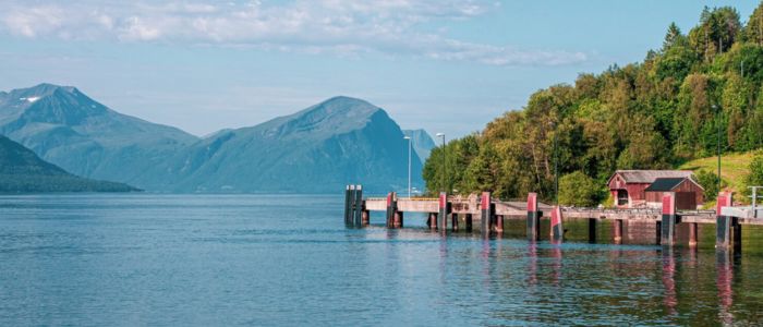 A scenic pier with a boat in the water, surrounded by majestic mountains in the background.