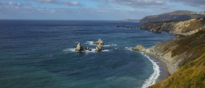 Aerial view of the Pacific Ocean coastline, showcasing waves crashing against rocky shores and sandy beaches.