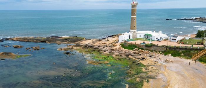 A lighthouse stands on the coast, overlooking the ocean with waves crashing nearby.