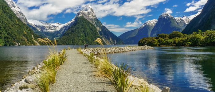 A scenic path leads to a tranquil lake, framed by majestic mountains in the background.