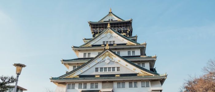Elegant Japanese castle with ornate multi-tiered roofs, adorned with intricate details, set against a clear blue sky, conveying a sense of historic grandeur.