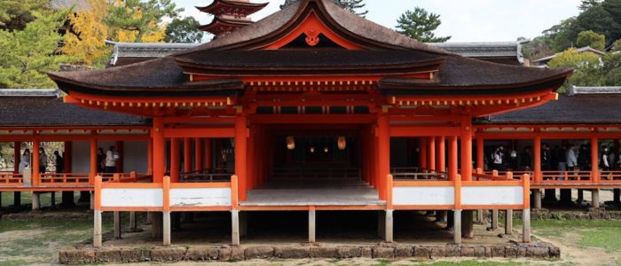 Traditional Japanese temple with vibrant red columns and ornate roofs on a raised platform. Surrounded by lush greenery, creating a serene atmosphere.