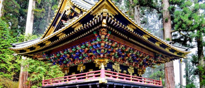 Ornate Japanese temple with intricate gold and colorful carvings, surrounded by tall, lush trees. The scene conveys serenity and cultural richness.