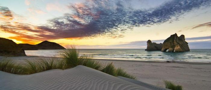 A serene beach at sunset, featuring soft sand dunes and scattered rocks against a colorful sky.